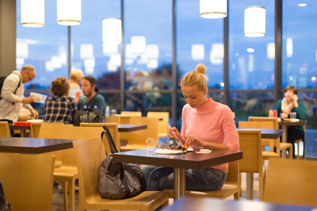 Young female traveler eating pizza in airport restaurant while waiting for late night flight departure.